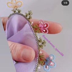 a hand holding a piece of cloth with beading on it's side and two butterfly pins in the middle