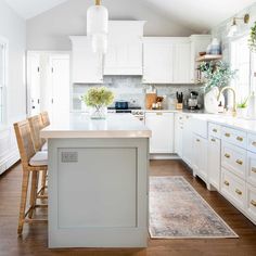 a kitchen with white cabinets and wooden floors, an island in the middle is flanked by two bar stools