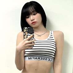 a woman with short black hair is looking at her cell phone while wearing a striped top