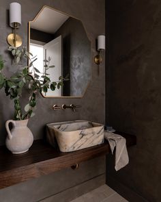 a bathroom sink sitting under a mirror next to a vase with a plant in it