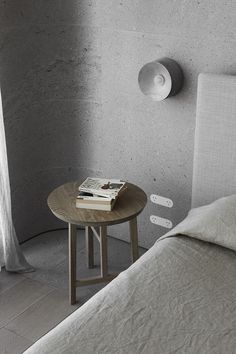 a small table with a magazine on it next to a bed in a room that has concrete walls