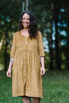 a woman standing in the grass wearing a dress with flowers on it and smiling at the camera