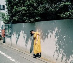 a woman leaning against a wall on the side of a street with her head in her hands