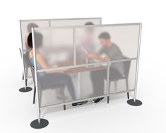 two people sitting at a table in an office cubicle with privacy screens on each side