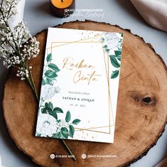 the wedding card is sitting on top of a wooden slice with flowers and greenery