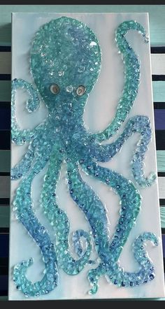 an octopus made out of glass beads on a white board with blue strips in the background