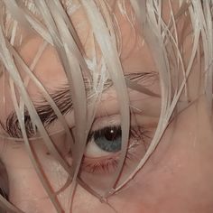 a woman's eye with long blonde hair on top of her head and blue eyes