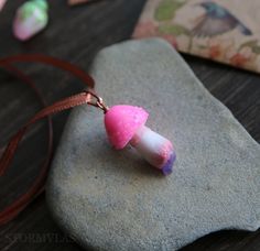 two pink and white necklaces sitting on top of a rock next to a brown cord