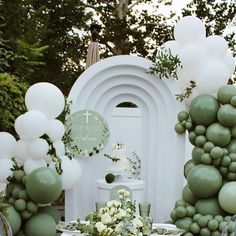 a table topped with lots of balloons and greenery next to a white arch in the background