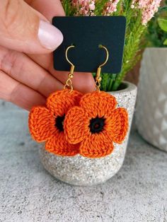 a pair of orange crocheted flower earrings with black centers in front of a plant