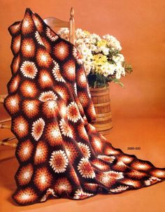 a crocheted blanket sitting on top of a chair next to a vase with flowers