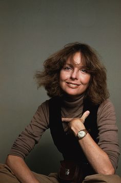 a woman sitting on the floor with her hand up to her chest and smiling at the camera