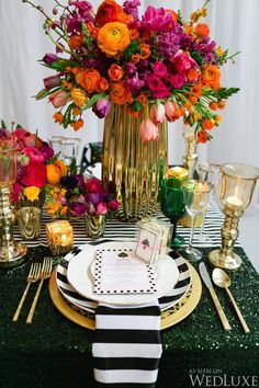 the table is set with black and white plates, goldware, and colorful flowers