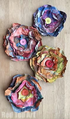 three paper flowers with buttons on them sitting on a wooden table next to each other