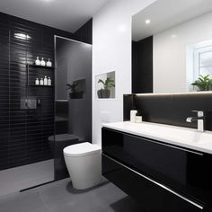 a black and white bathroom with a toilet, sink, shower stall and plants on the wall