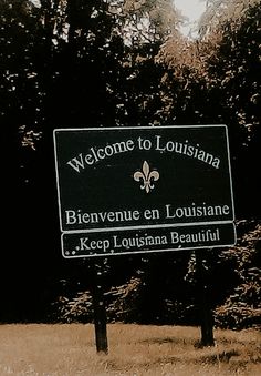 a black and white sign sitting in the middle of a field next to some trees