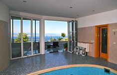 an indoor swimming pool with sliding glass doors leading out onto the water and mountains in the distance