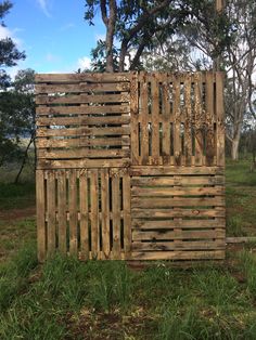 a wooden structure sitting in the middle of a field next to some trees and grass