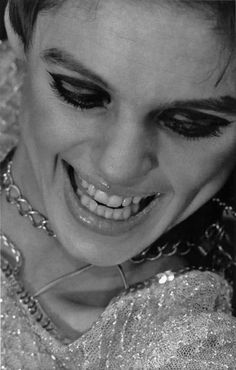 black and white photograph of a woman with makeup on her face, smiling at the camera