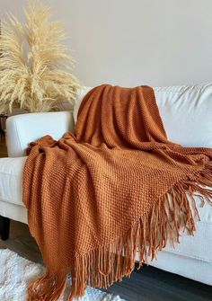 a white couch with an orange blanket on it next to a potted grass plant