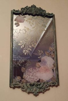 a mirror hanging on the wall with flowers and leaves in it's reflection,