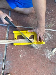 a man holding a pair of scissors on top of a yellow tool box next to a hammer