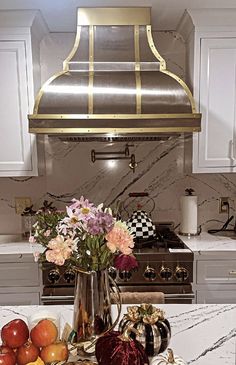 a kitchen with marble counter tops and an oven hood over the stove, filled with fruits and vegetables