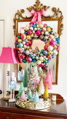 a christmas wreath on top of a dresser next to a pink lamp