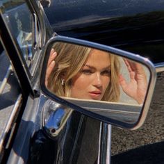 a woman's reflection in the side view mirror of a car as she holds her hand up to her head