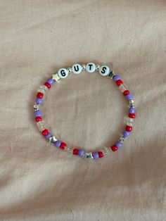 A hand-crafted glass bead friendship bracelet highlighting Olivia Rodrigo's album, GUTS! A simple and cute way to show off your favorite song or a great concert accessory!  This bracelet is made with Czech glass beads, plastic letter beads, plastic spacer beads, and is on an elastic thread measured at about 10 inches in length for a relaxed/loose fit. If you would like the bracelet you order to be smaller or larger, please leave the requested size in inches in the personalization box!  All bracelets are made to order and are typically shipped out within 1-3 business days unless otherwise stated. Olivia Friendship Bracelet, Guts Friendship Bracelet, Ariana Grande Bracelet, Olivia Rodrigo Friendship Bracelet, Olivia Rodrigo Bracelets, Olivia Rodrigo Bracelet Ideas, Friendship Bracelets Simple, Olivia Bracelet, Olivia Rodrigo Bracelet