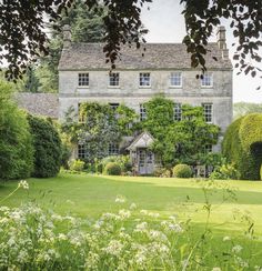 an old stone house surrounded by trees and flowers in the country side yard with lush green grass