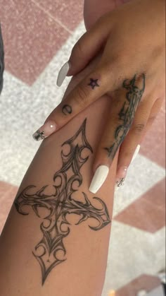 a woman's hand with a cross tattoo on her left arm and white nails