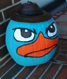 a blue pumpkin with an angry bird painted on it's face and hat sitting next to a brick wall