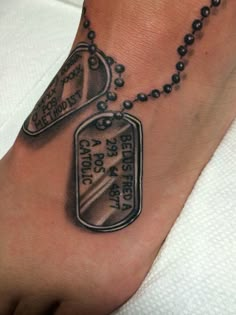 a tattoo on the foot of a person with a dog tag and chain attached to it