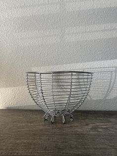 a wire basket sitting on top of a wooden table in front of a white wall