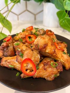 chicken wings with peppers and herbs on a black plate next to a potted plant