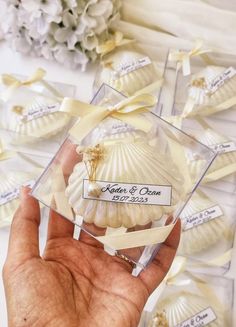 a hand holding a small glass box with seashells in it and ribbons on the sides