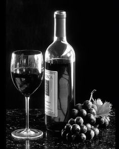 a bottle of wine and some grapes on a table with a glass next to it