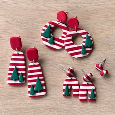 three pairs of red and white striped earrings with green christmas trees on them, sitting on a wooden surface