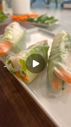 two rolls with carrots and lettuce wrapped in plastic on a white plate