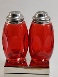 two red salt and pepper shakers sitting on top of a silver block with a white background