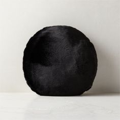 a black round pillow sitting on top of a white table next to an empty wall