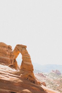 a person standing on top of a rock formation with an arch in the middle and mountains in the background