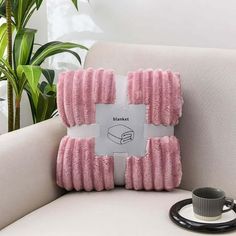 a pink pillow sitting on top of a white couch next to a cup and saucer