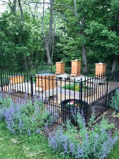 a fenced in area with purple flowers and plants around it, surrounded by trees