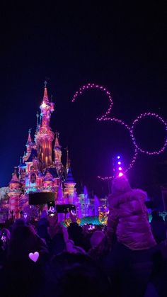 the disneyland castle is lit up at night with purple lights and people standing in front