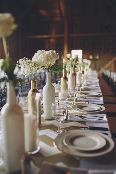 the table is set with wine bottles, plates and flowers in vases on it