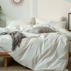 an unmade bed with white and grey striped comforter, pillows and throw blanket