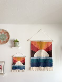 two woven wall hangings on the wall next to a potted plant and pictures