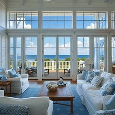 a living room filled with furniture and large windows overlooking the ocean on a sunny day